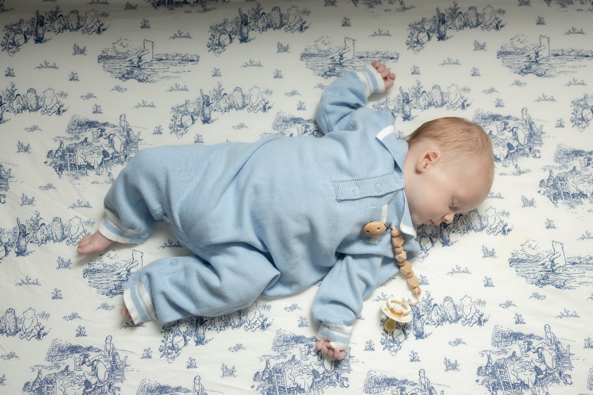 Baby in a blue onesie lying on a patterned blanket