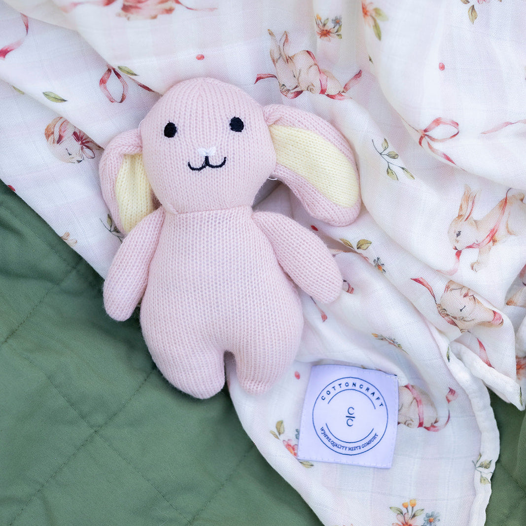 Pink knitted bunny toy on a floral blanket with a green fabric background