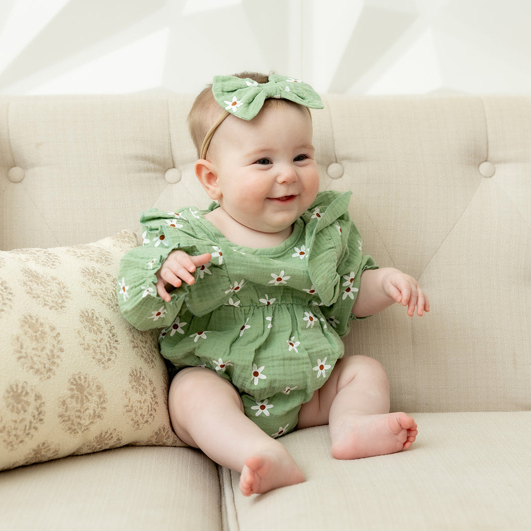 Baby in a green outfit sitting on a beige couch with a white background