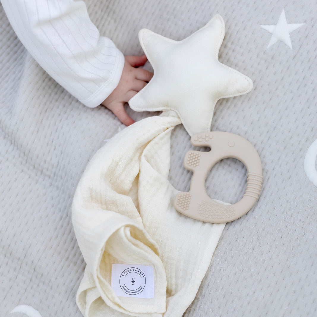 Baby holding a star-shaped toy with a soft blanket on a gray surface