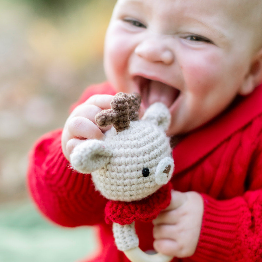 Baby in a red sweater holding a small knitted toy outdoors