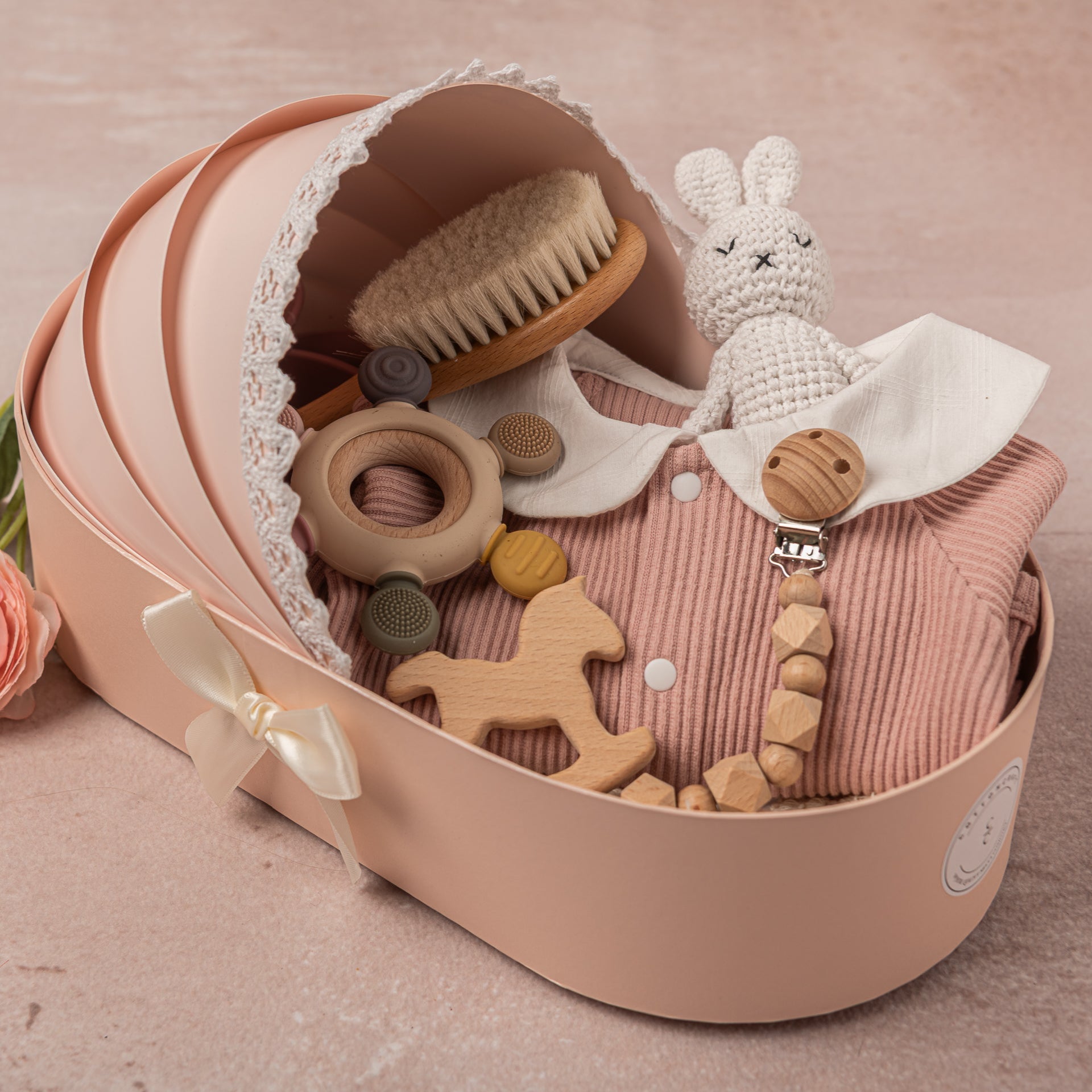 Luxury baby girl gift set featuring soft pink and white 100% cotton outfits, a fringed swaddle, leather baby shoes, hand-knitted bunny plush, and sustainable wooden and silicone toys, elegantly displayed.