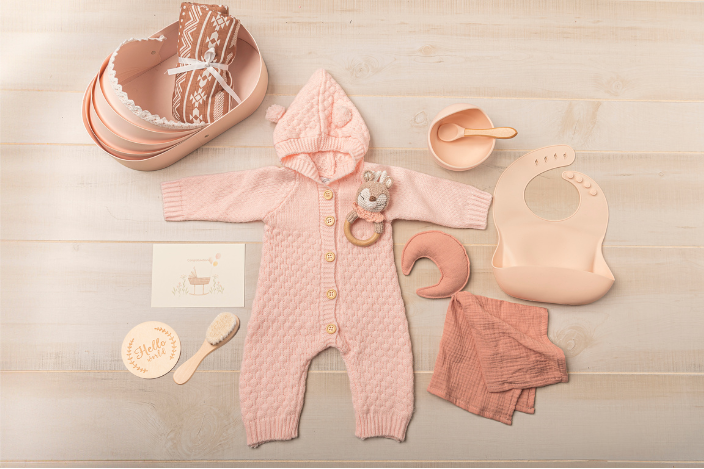 Pink baby romper with accessories on a wooden surface